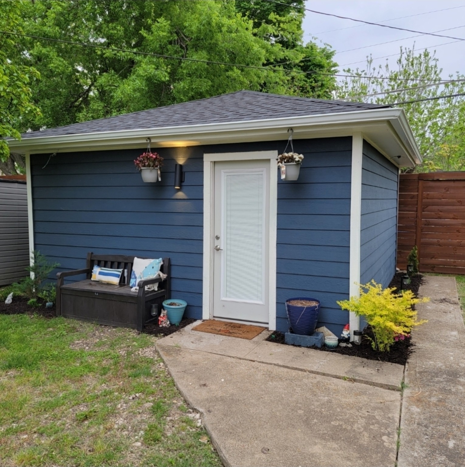 After: the garage with blue siding, white trim, a glazed door, exterior light and planting beds.