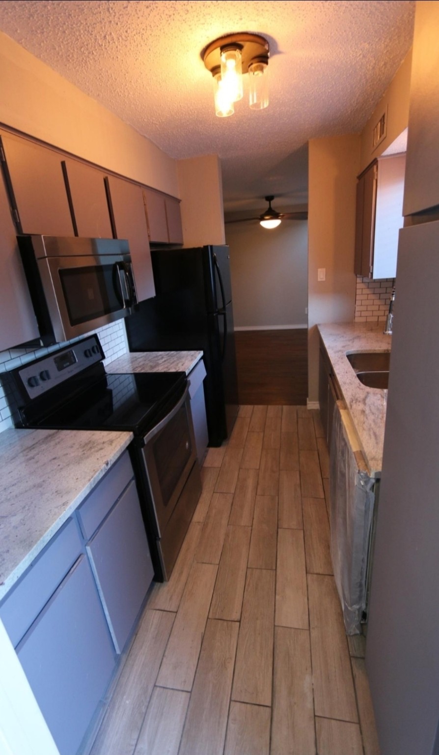 After: a galley kitchen with gray cabinets, light counters, a tile backsplash and black appliances.