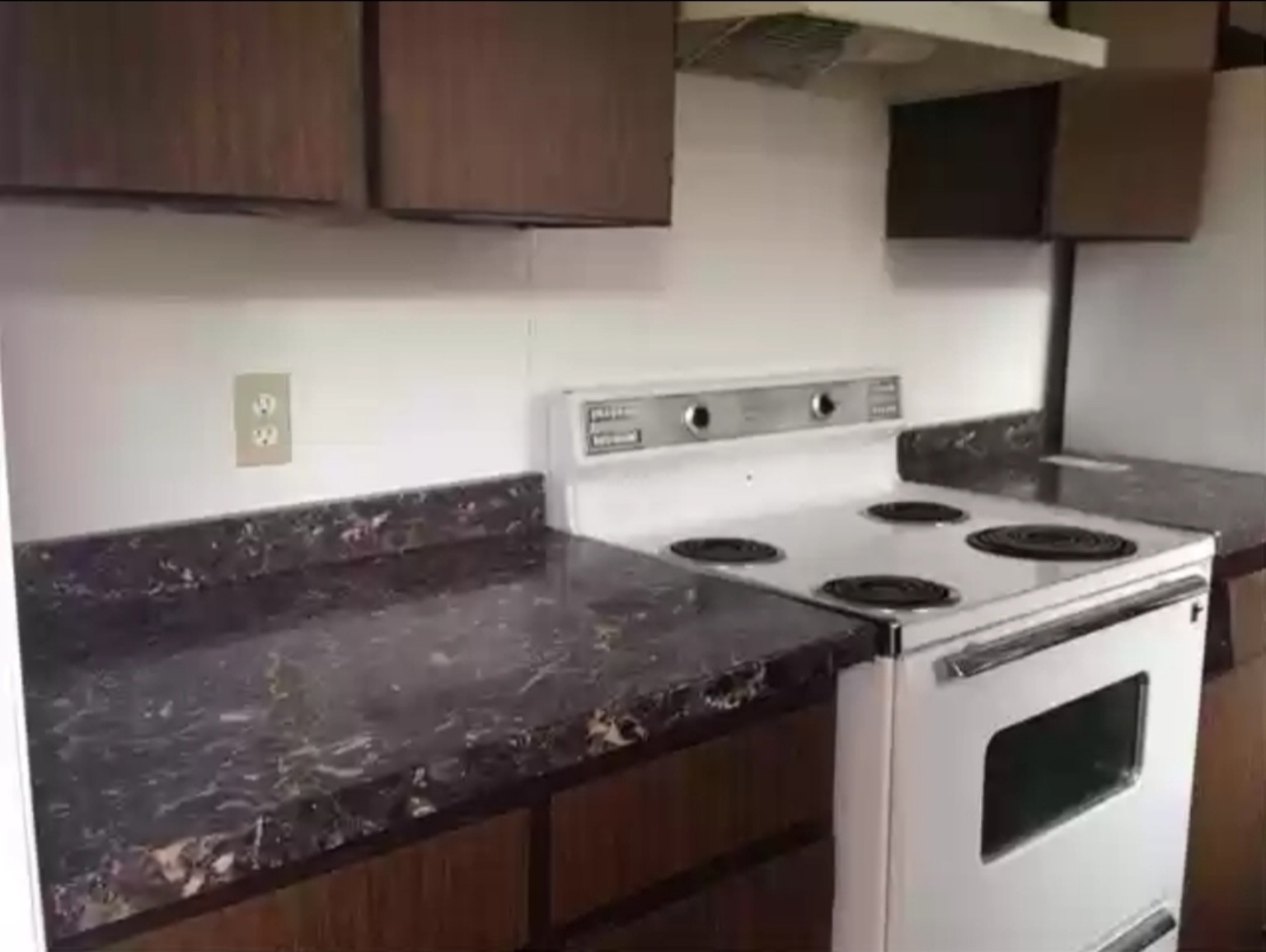 Before: dark wood kitchen cabinets, dark counters and a white electric range.