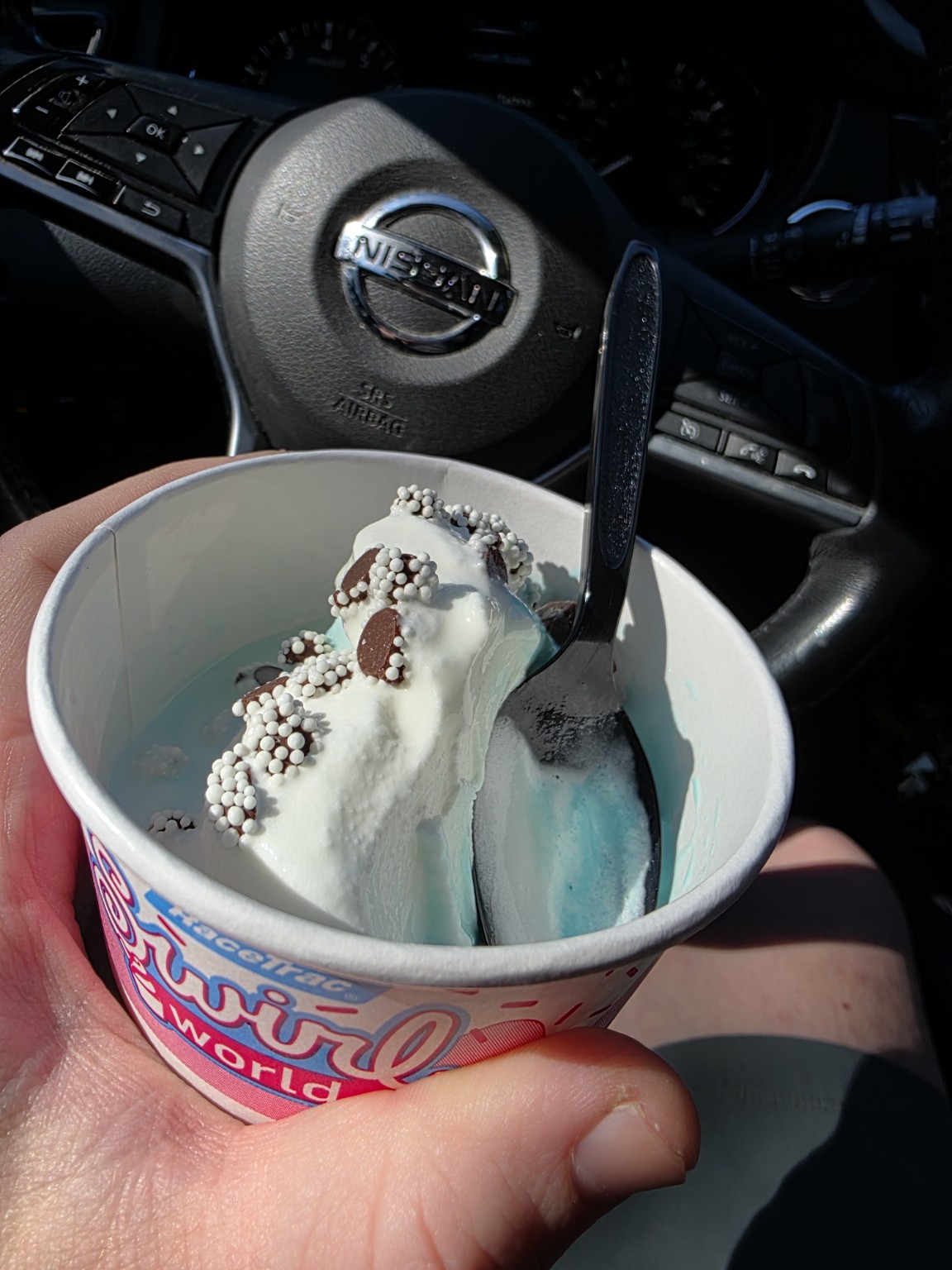 A cup of blue ice cream with chocolate toppings held inside a parked car