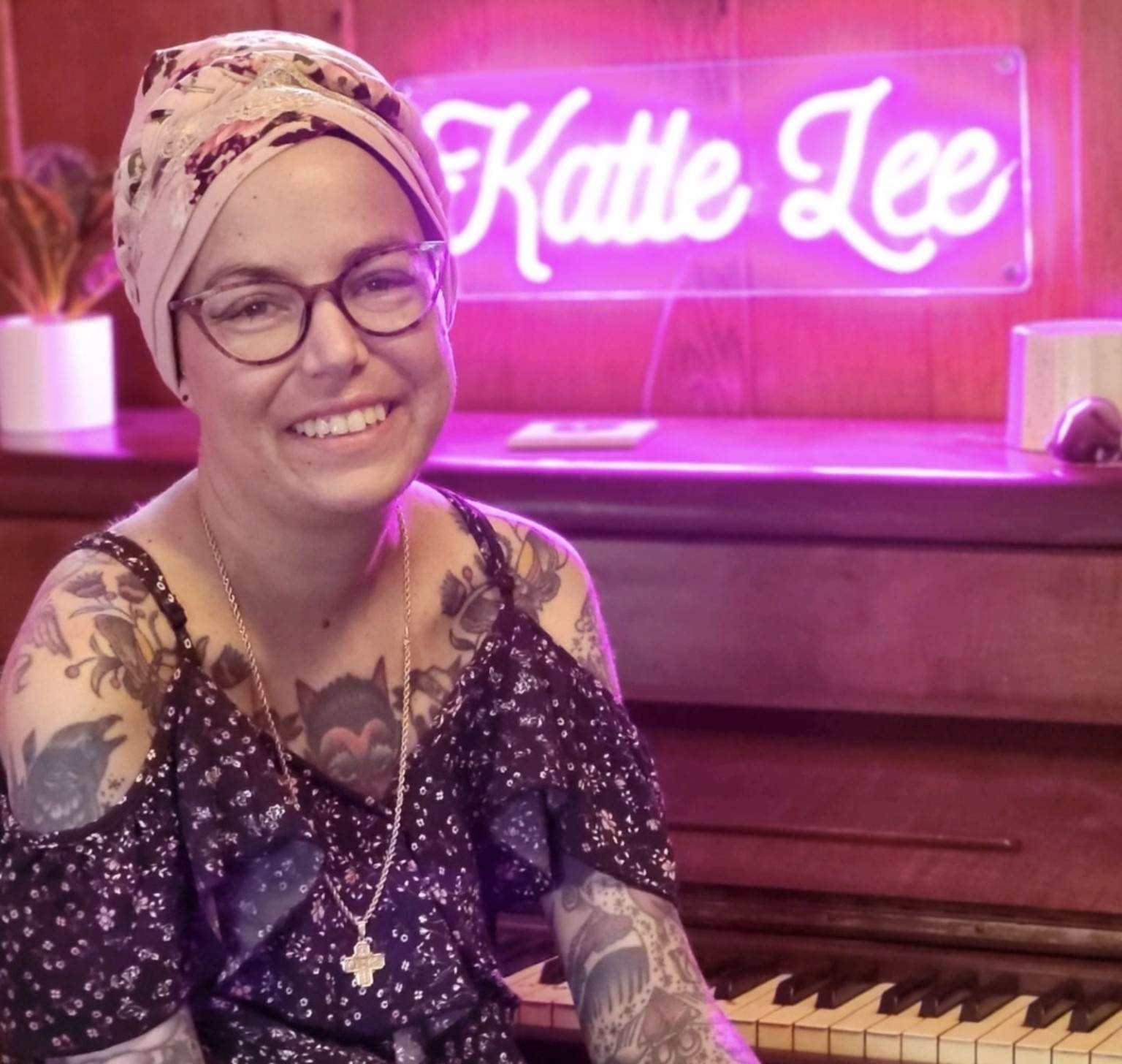 Katie Lee smiling beside the piano and neon Katie Lee sign
